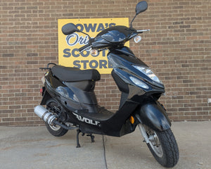 Black scooter parked in front of a brick wall with a sign for 'Iowa's Original Scoot Store'.